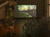 A large dark space shining on different mono bloc chairs positioned in front of a screen projection of a woodland at dawn or dusk.